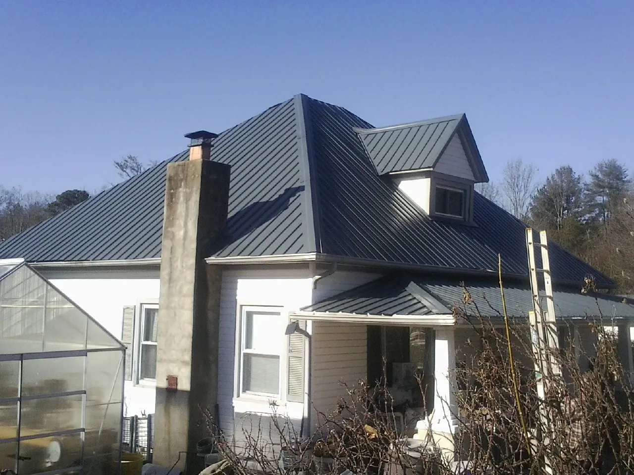 Dark blue standing seam metal roof on a white farmhouse with dormer — Slate & Tile Roof Repair by Roofing Brothers in Logansport