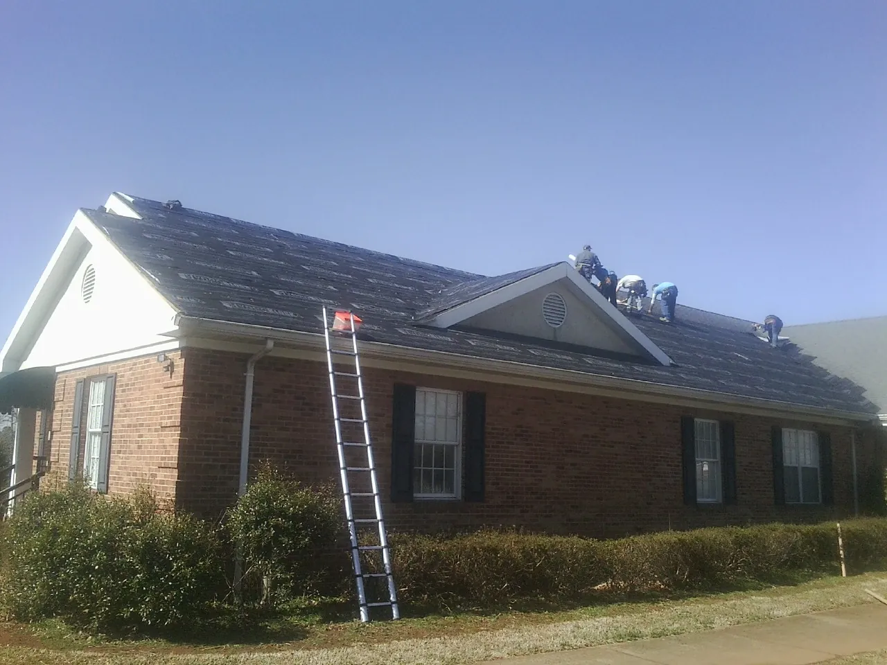 Crew tearing shingles off a brick ranch roof with a ladder set — Emergency Roof Repair work by our crew in Logansport