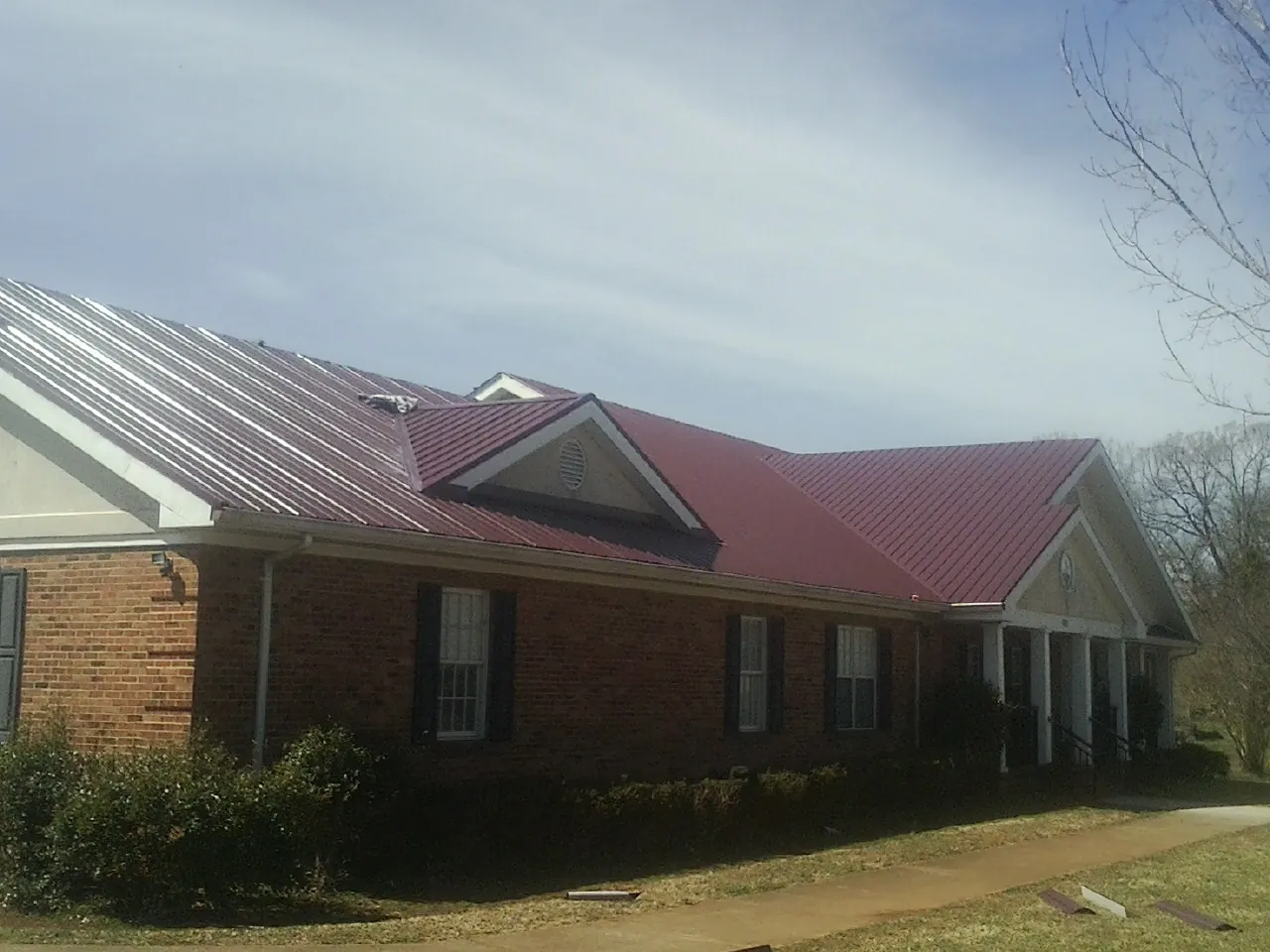 Red metal roof with gabled entries on a long brick building, from a Hail Damage Roof Repair job in Logansport