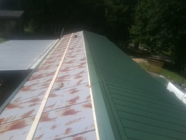 Old rusted panels beside newly installed green metal roofing — Wind Damage Roof Repair by Roofing Brothers in Logansport