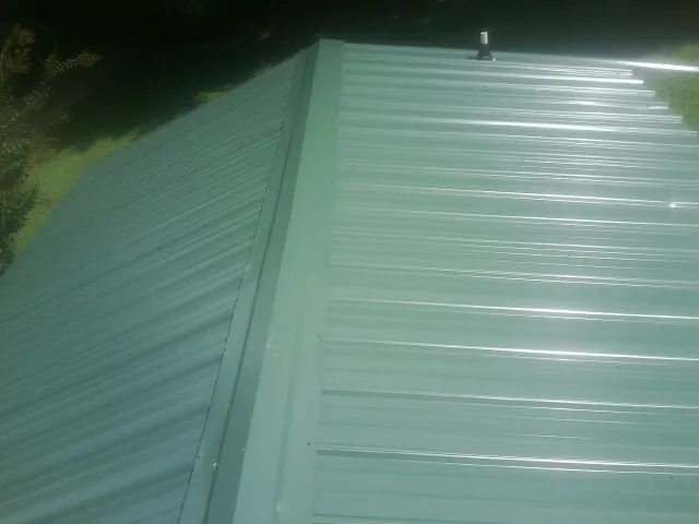 New green metal panels meeting at the ridge of a roof — Flat Roof Repair work by our crew in Logansport