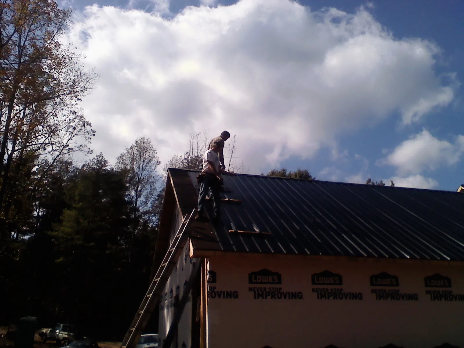 Roofer fastening dark metal panels high against a cloudy sky, from a Roof Inspection job in Logansport