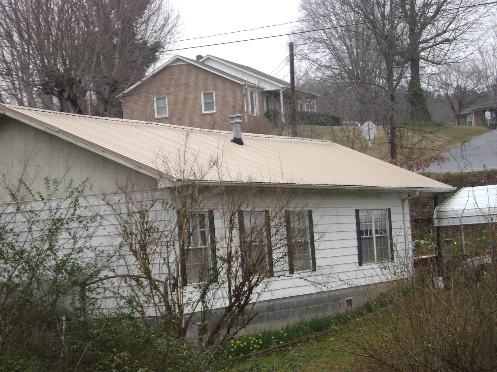 Tan metal roof on a white sided house set into a hillside — Commercial Roofing by Roofing Brothers in Logansport