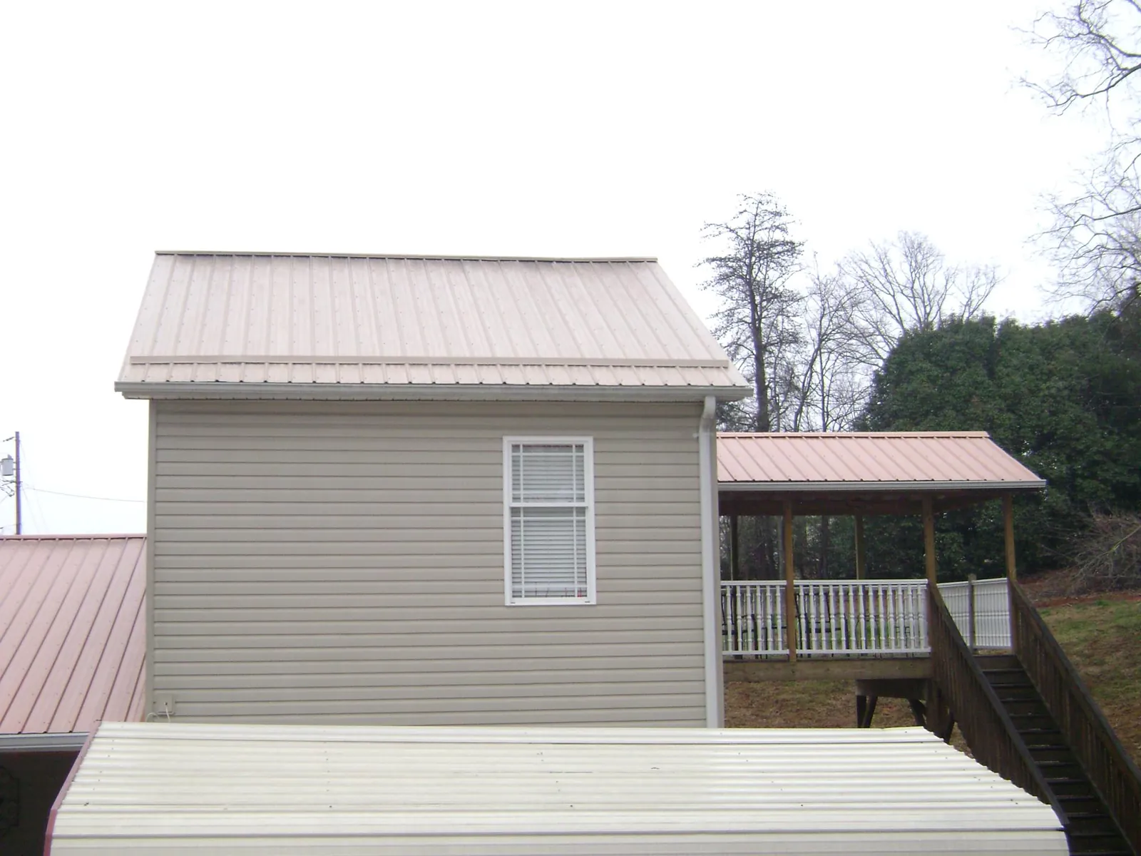 Tan metal roofs on a two story addition and attached porch, from a Roof Replacement job in Logansport